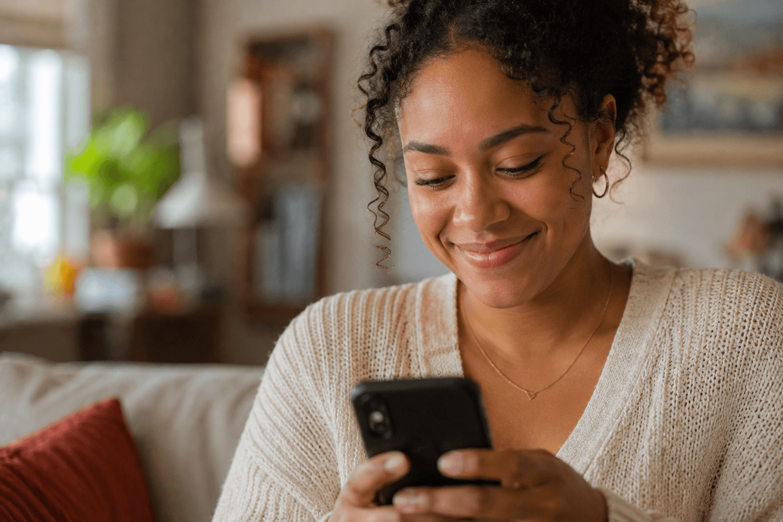 A young woman smiling warmly at her phone as she sets up her family’s newsletter